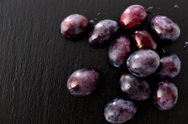 Siyah taş tabakta taze mor erikler