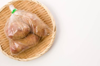 Taze kırmızı derili patatesler, beyaz arka planda bambu kevgir üzerinde plastik torba içinde toprak. 