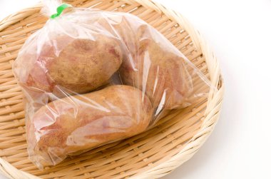 Taze kırmızı derili patatesler, beyaz arka planda bambu kevgir üzerinde plastik torba içinde toprak. 