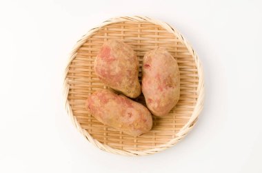 Taze kırmızı derili patatesler, beyaz arka planda bambu kevgire toprak sürülmüş.