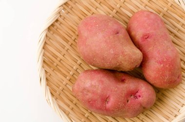 Beyaz arka planda bambu kevgir üzerinde taze kırmızı derili patates. 