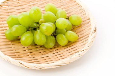 Taze yeşil tohumsuz üzümler beyaz arkaplanda bambu süzgeci üzerinde
