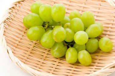 Taze yeşil tohumsuz üzümler beyaz arkaplanda bambu süzgeci üzerinde