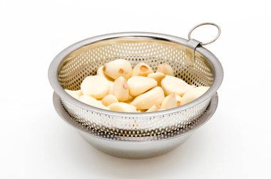 Beyaz arka planda paslanmaz çelikten kevgirle soyulmuş sarımsak.