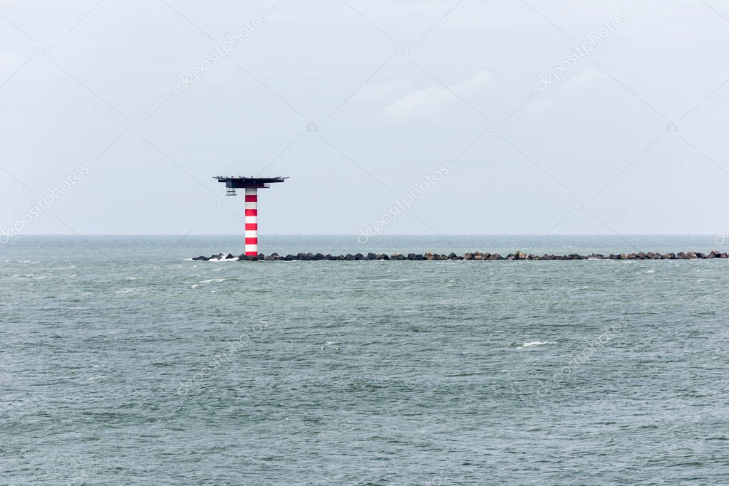 The red and white striped lighthouse with heliplatform at the entrance of the Port of Rotterdam in the Netherlands. The lighthouse is situated at the end of a pier with concrete wave breakers.