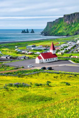 View of basalt stacks Reynisdrangar, black sand beach, church and city of Vik, South Iceland, summer time clipart