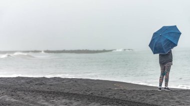Vik, South Iceland, yaz saati yakınındaki siyah kum plajda Reynisdrangar, şemsiye ile yalnız kız