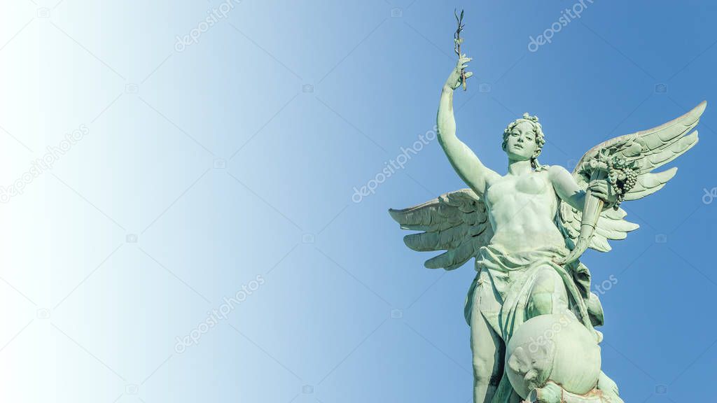 Top roof statue of sensual renaissance era angel with wings in front of blue sky in Vienna, Austria