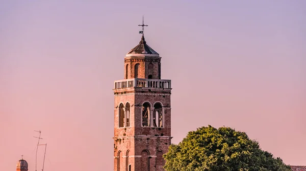 Technological contrast over aged bell tower with cross and telecommunication antennas, Venice, Italy