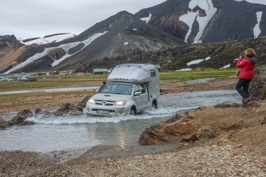 4WD arabası, renkli gökkuşağı volkanik Landmannalaugar dağlarında her mevsim binlerce turist ve yürüyüşçüyle büyük bir kamp alanının yanındaki nehri geçiyor.