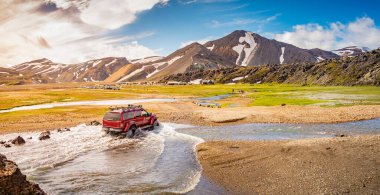 4WD arabası, renkli gökkuşağı volkanik Landmannalaugar dağlarında her mevsim binlerce turist ve yürüyüşçüyle büyük bir kamp alanının yanındaki nehri geçiyor.