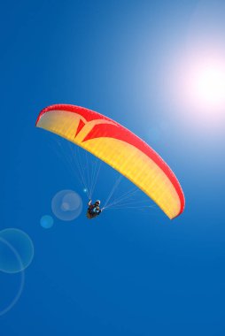 Güzel sarı ve kırmızı paraglider mavi gökyüzünde uçuyor, ışık efektiyle ve boşluğu kopyalayarak.