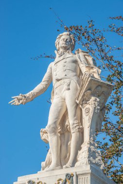 Güneşli bir günde Avusturya, Viyana 'nın tarihi merkezinde, Neue Burg ve Hofburg Sarayı yakınlarındaki Palmenhaus' un önündeki Mozart anıtının üzerinde ılık bir günbatımı güneşli bir günde mavi gökyüzü sonbahar renklerinde.