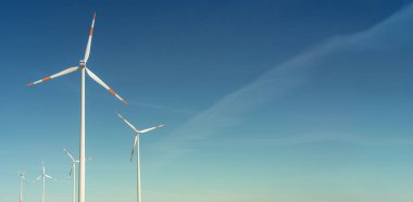 Elektrik enerjisi üretmek için büyük rüzgar türbinleri, mavi gökyüzünde yeşil eko-dostluk enerjisi, günbatımı sıcak renkler ve metin alanı için fotokopi alanı