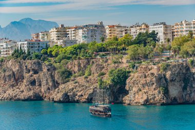 Akdeniz 'de Antalya yakınlarındaki sahil ve sahil kenarındaki şelale manzarası ve geçmişten gelen bir korsan yelkenliye benzeyen büyük tur teknesi, Antalya, Türkiye