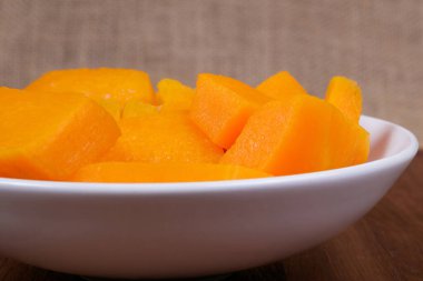 Tahta masadaki kasede balkabağı parçaları ve çuval bezi arka planda.