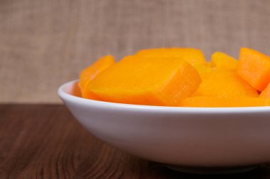 Tahta masadaki kasede balkabağı parçaları ve çuval bezi arka planda.