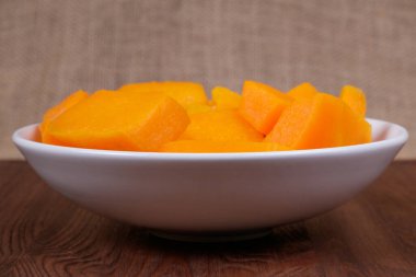 Tahta masadaki kasede balkabağı parçaları ve çuval bezi arka planda.