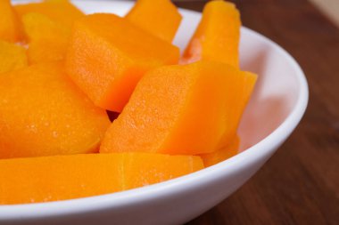 Tahta masadaki beyaz kasede donmuş balkabağı parçaları..