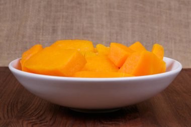 Tahta masadaki kasede balkabağı parçaları ve çuval bezi arka planda.