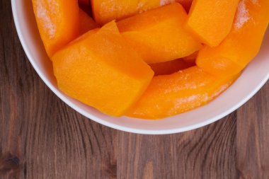 Tahta masadaki beyaz kasede donmuş balkabağı parçaları..