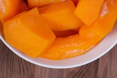 Tahta masadaki beyaz kasede donmuş balkabağı parçaları..