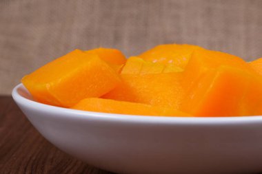 Tahta masadaki kasede balkabağı parçaları ve çuval bezi arka planda.