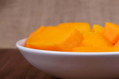 Tahta masadaki kasede balkabağı parçaları ve çuval bezi arka planda.