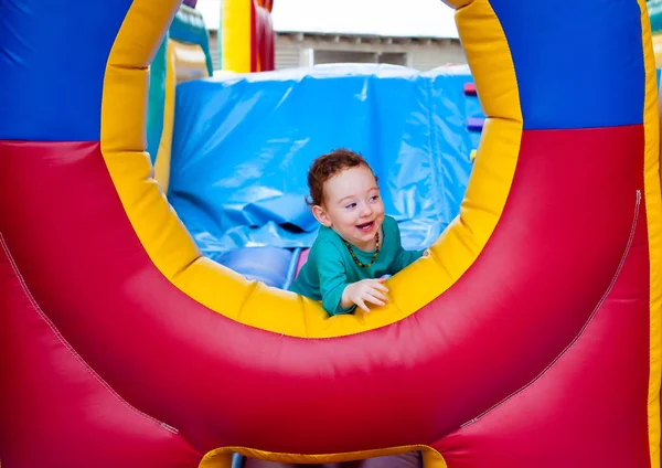 stock image Curious funny toddler peeking out from colorful trampoline castle