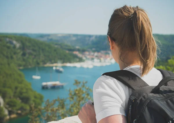 Female tourist with backpack looking at city near the lake.