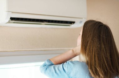 Women dying from the heat standing in front of the air conditioner. clipart