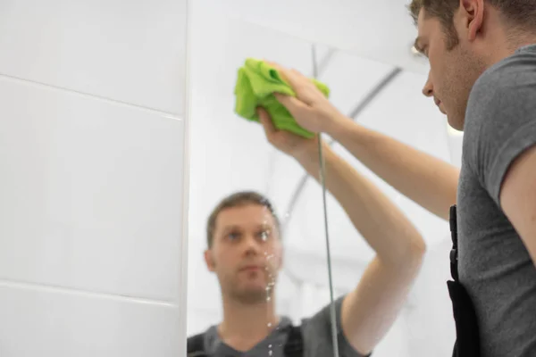 クリーニングのサービス コンセプトです バスルームのガラス キャビネットをクリーニング男 — ストック写真