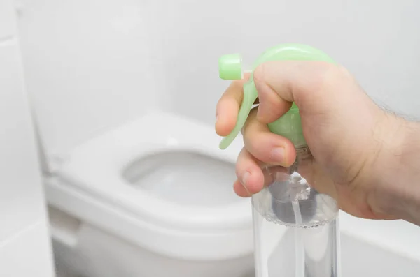 Male hand spraying toilet air freshener at home.