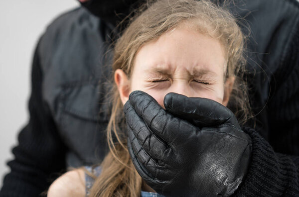 Man's hand covering mouth of scared young girl.
