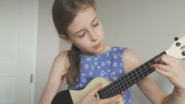 かわいい女の子が自宅にウクレレを弾くことを学ぶ — ストック動画