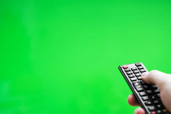 Male hand with TV remote control over green screen. Place for your advertisement. — Stock Photo, Image