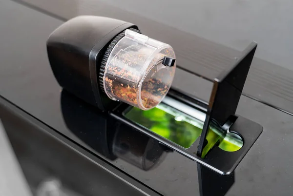 Automatisk fisk feeder stående på locket till akvarium. — Stockfoto