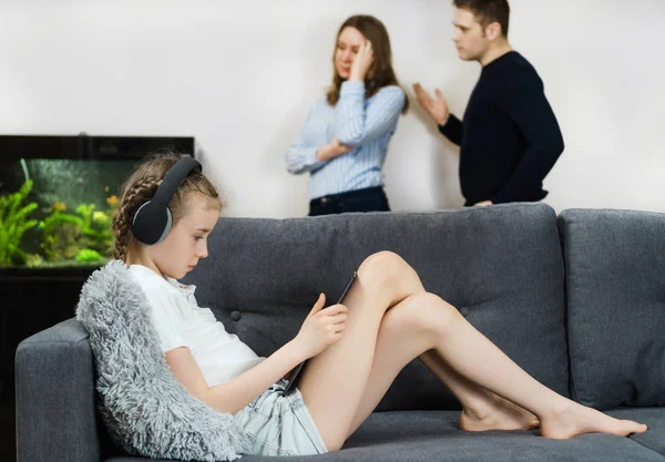 Niña en los auriculares usando tableta PC mientras sus padres en disputa en el fondo . —  Fotos de Stock