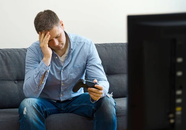 Homem perturbado sentado no sofá com gamepads . — Fotografia de Stock