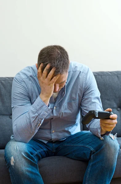 Homem perturbado sentado no sofá com gamepads . — Fotografia de Stock