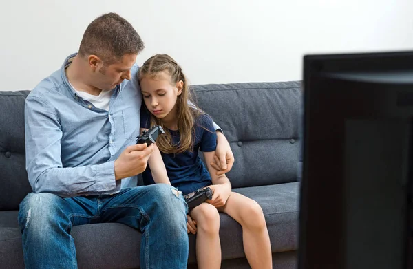 Sur far og datter sitter på sofaen med spilleautomater. . – stockfoto