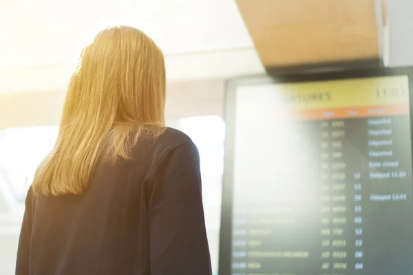 Mujer en frente del tablero de información de vuelo, comprobando su vuelo . — Foto de Stock