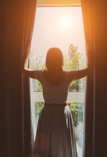 Woman opening curtains in the hotel room at sunny morning.
