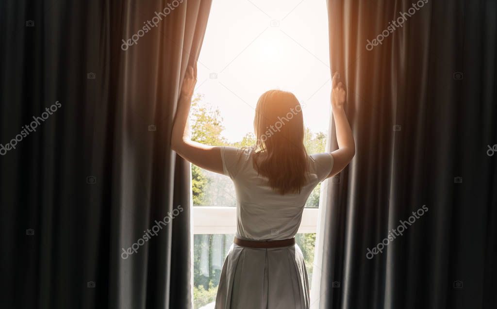 Woman opening curtains in the hotel room at sunny morning.