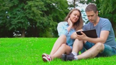 Yaz mevsiminde kadın ve erkek parkta tablet kullanıyor..