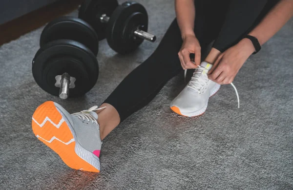 Egzersizden önce ayakkabı bağı bağlayan bir kadın. Evde fitness eğitimi kavramı.