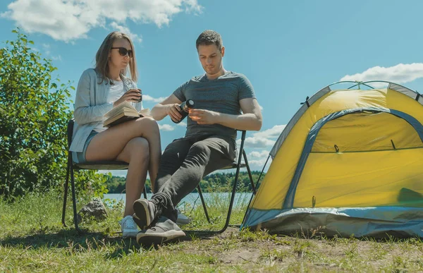 男人和女人在湖边露营帐篷边的热水瓶里喝茶 — 图库照片