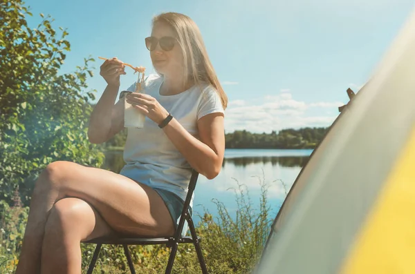 女人在湖边帐篷边吃方便面 — 图库照片