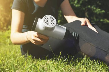 Antrenmandan sonra masaj perküsyon cihazıyla kadın bacağına masaj yapıyor.