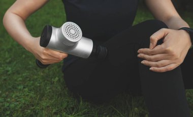 Antrenmandan sonra masaj perküsyon cihazıyla kadın bacağına masaj yapıyor.